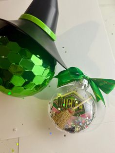 a glass ornament with a green bow on it and a witch hat hanging from the top