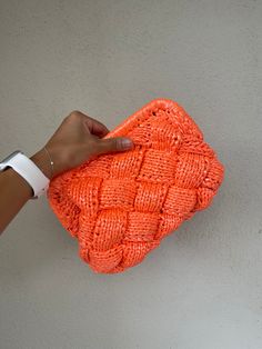 a person holding an orange knitted purse