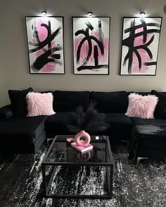 a living room with black couches and pink pillows on the rugs, two framed pictures above them