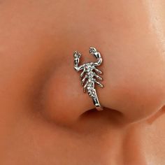 a woman's nose with a small silver scorpion piercing on the top of it