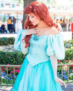 a woman with red hair wearing a blue dress and holding her hand on her shoulder