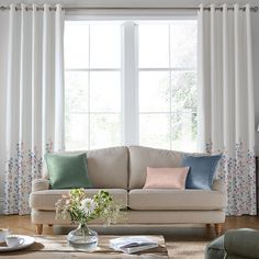 a living room filled with furniture and pillows on top of a wooden floor next to a window