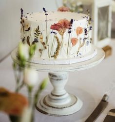 a white cake with flowers on it sitting on top of a table next to silverware