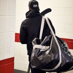 a man carrying a black duffel bag in front of a white brick wall,