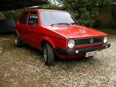 a red car is parked in the gravel