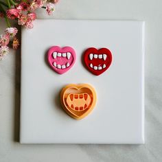 three cookie molds shaped like mouths and teeth on a white plate next to pink flowers