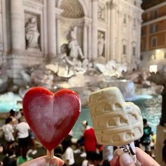 two heart shaped lollipops being held in front of a fountain