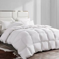 a white comforter on a bed in a room with hardwood floors and windows,