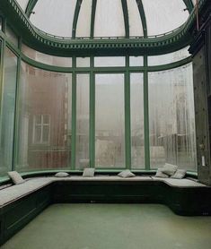 the inside of a green building with lots of windows and pillows on it's seat