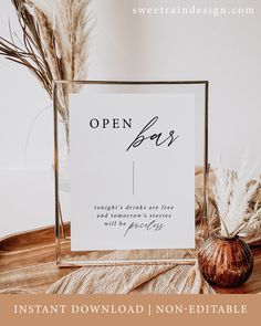 an open box sign sitting on top of a table next to a vase filled with dry grass