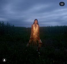 a woman standing in the middle of a field at night with lights on her body