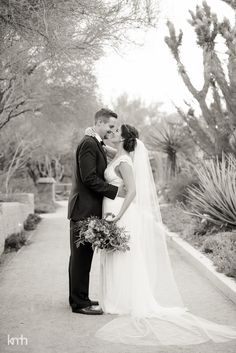 a bride and groom standing together in front of cactus trees at their wedding day, black and white photo