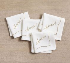 three white napkins with gold lettering on them sitting on a wooden table next to each other