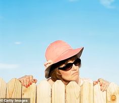 a woman wearing sunglasses and a pink hat leaning on a wooden fence with her hands over the top