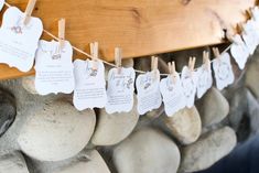 some paper tags are hanging from clothes pins on a line with rocks and wood in the background