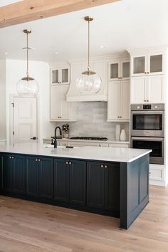 a large kitchen with white cabinets and black island counter tops, two pendant lights over the sink