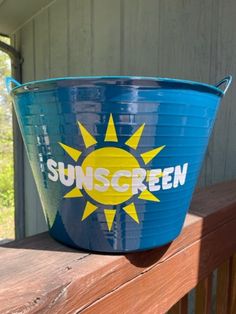 a blue bucket with the words sunscreen on it is sitting on a wooden porch