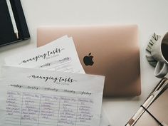 a laptop computer sitting on top of a desk next to some paper and pen with writing on it