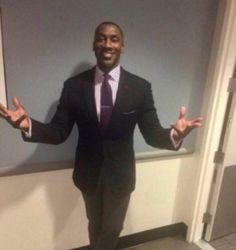 a man wearing a suit and tie standing in front of a wall with his hands out