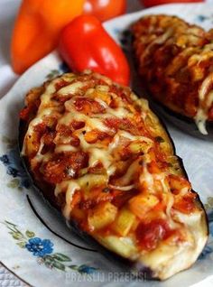 two stuffed eggplant halves on a plate with tomatoes and peppers in the background