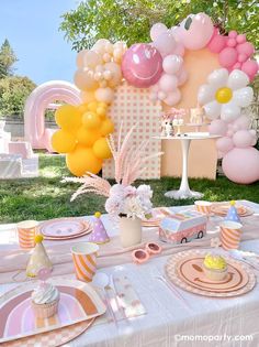 a table set up for a birthday party with balloons, plates and cupcakes