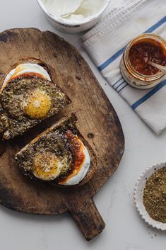 two pieces of bread on a cutting board with eggs and sauces next to it