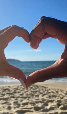 two hands making a heart shape on the beach