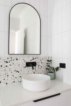 a white sink sitting under a large mirror in a bathroom next to a potted plant