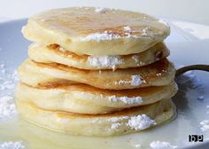 a stack of pancakes sitting on top of a white plate covered in powdered sugar