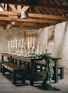 a long table with candles and greenery on it in the middle of a room