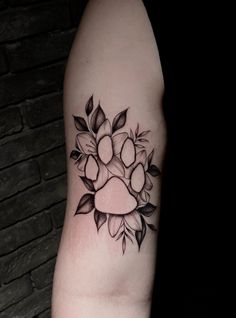 a black and white photo of a paw print tattoo on the left arm with leaves around it