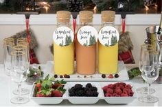 three bottles of liquid sitting on top of a table next to plates of berries and raspberries