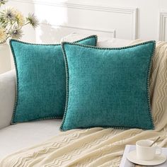 two teal pillows sitting on top of a bed next to a cup and saucer