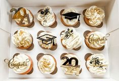 twelve cupcakes in a box decorated with white frosting and graduation decorations,