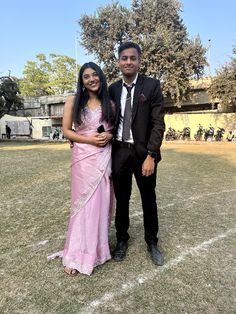 a man and woman in formal wear posing for the camera on a football field with trees in the background