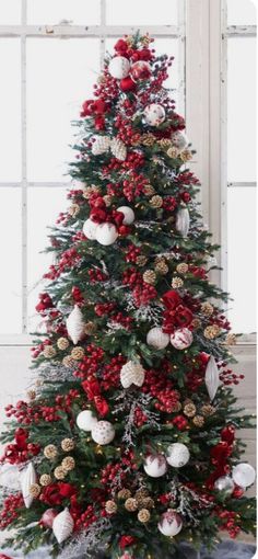 a decorated christmas tree with red and white ornaments on the top, in front of a window