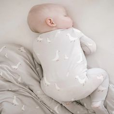 a baby laying on top of a bed covered in white sheets and blankets with birds printed on them