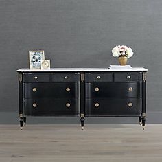 a black and white dresser with gold hardware on it's drawers next to a gray wall