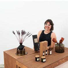 a woman sitting at a table with some vases and candles on top of it