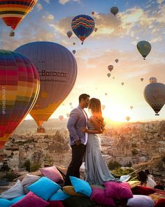 a man and woman standing in front of hot air balloons with the sun setting behind them