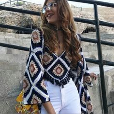 a woman wearing white pants and a patterned cardigan is posing for the camera with her hand on her hip