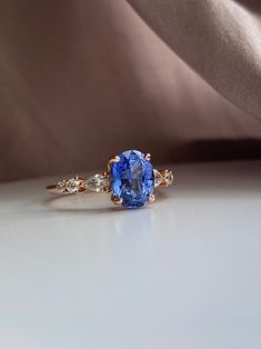 an oval blue sapphire and diamond ring on a white surface with a satin fabric in the background