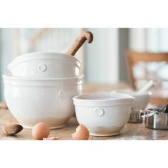 three white bowls sitting on top of a wooden table next to an egg grinder