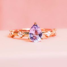 a close up of a ring with a pink stone on top and two white diamonds around it