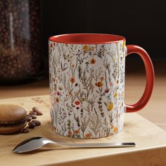 a coffee mug sitting on top of a wooden table next to a spoon and cookie