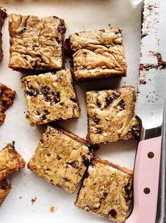 a cutting board topped with lots of brownies next to a pink handled knife on top of a table