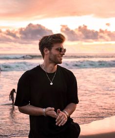 a man standing on top of a sandy beach next to the ocean with his hands in his pockets