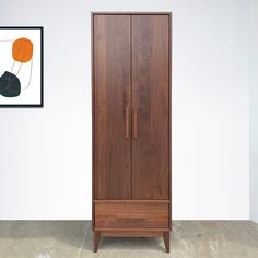 a tall wooden cabinet sitting next to a wall with a painting hanging on the wall