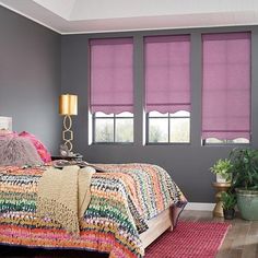 a bedroom with grey walls and pink roman shades on the windows, bed in foreground