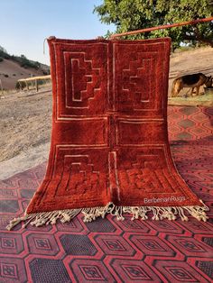 an old red rug is laying on the ground in front of a tree and some cows